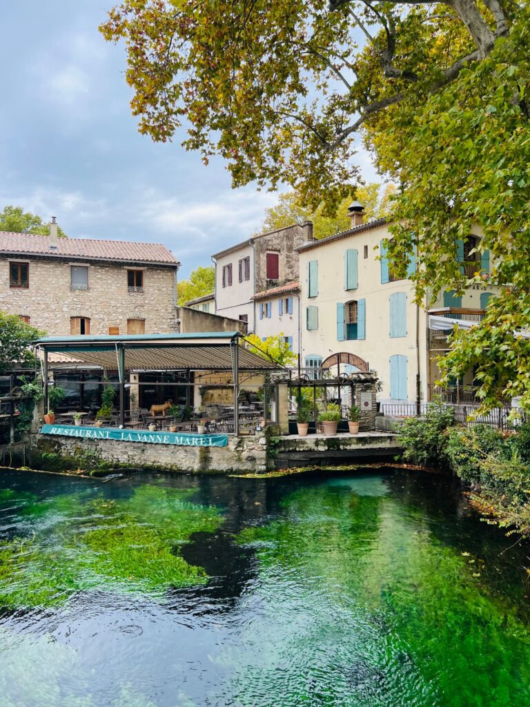 Une roue à aubes et des maisons au bord de l'eau verte de la Sorgue, à L'Isle-sur-la-Sorgue.